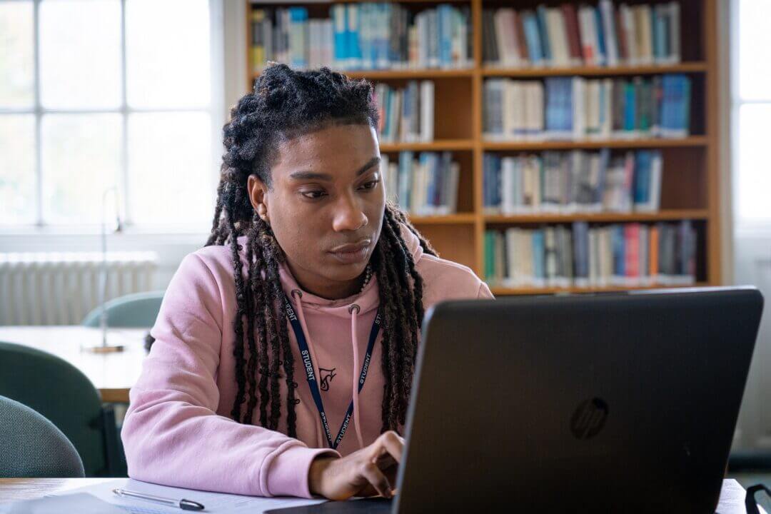 student studying at laptop with shelves of books in background